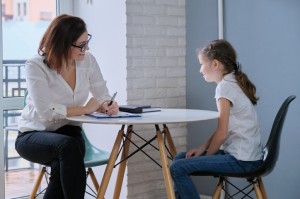 woman with notepad sits at table with young girl