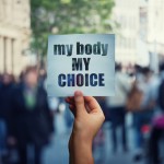 Feminist hands holding a protest banner with the message my body my choice over a crowded street. Human rights concept against fetus law and reproductive justice. Stop discrimination and injustice