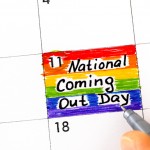 Woman fingers with pen writing reminder National Coming Out Day in calendar. October 11