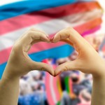 hands making hear shape over transgender flag in background