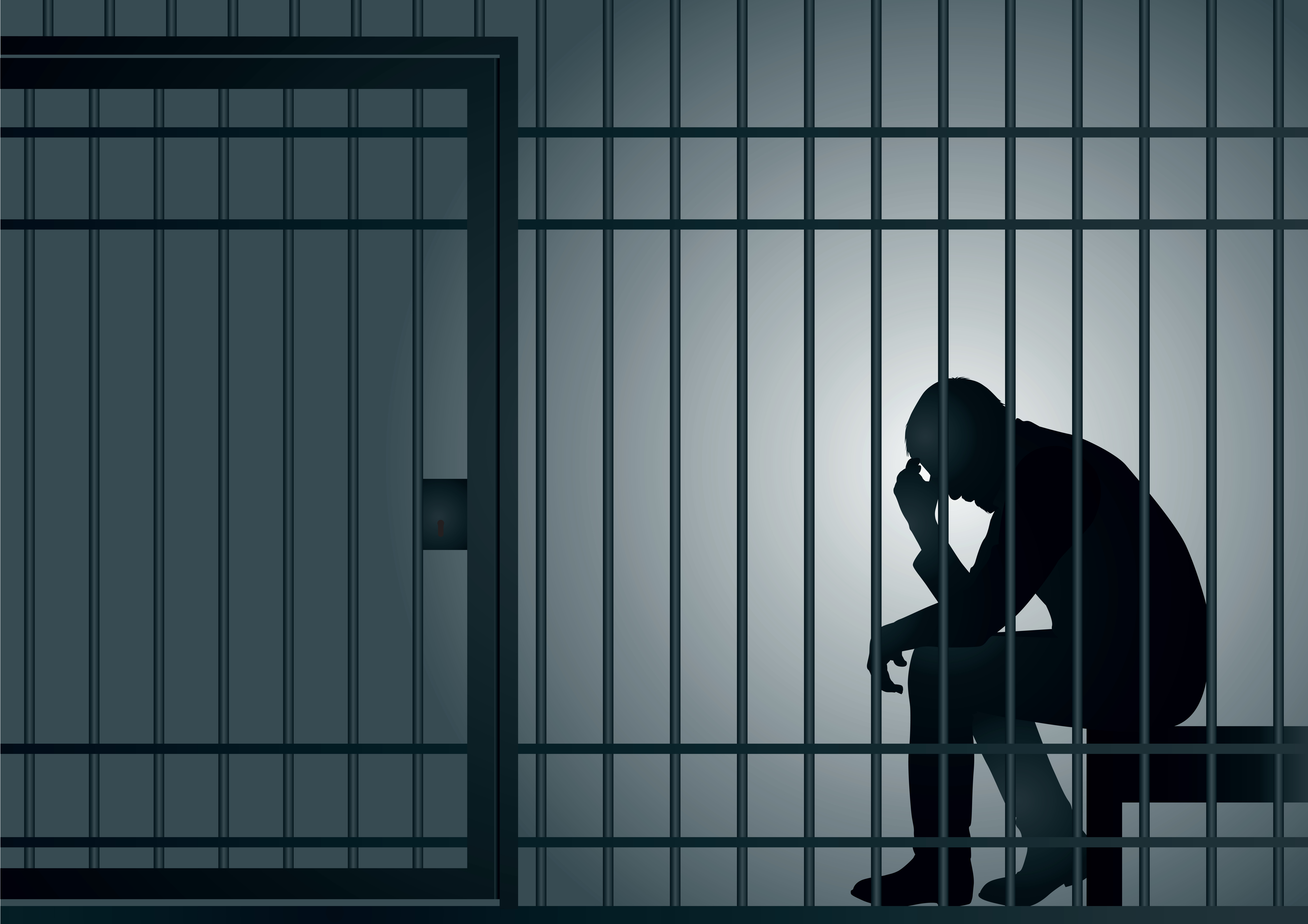 person sitting in a jail cell holding their head in their hands