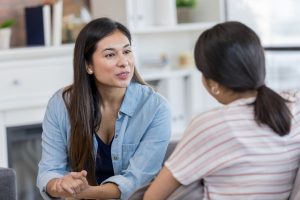 The mid adult mom speaks earnestly to her teen daughter after school while they sit together on the couch.