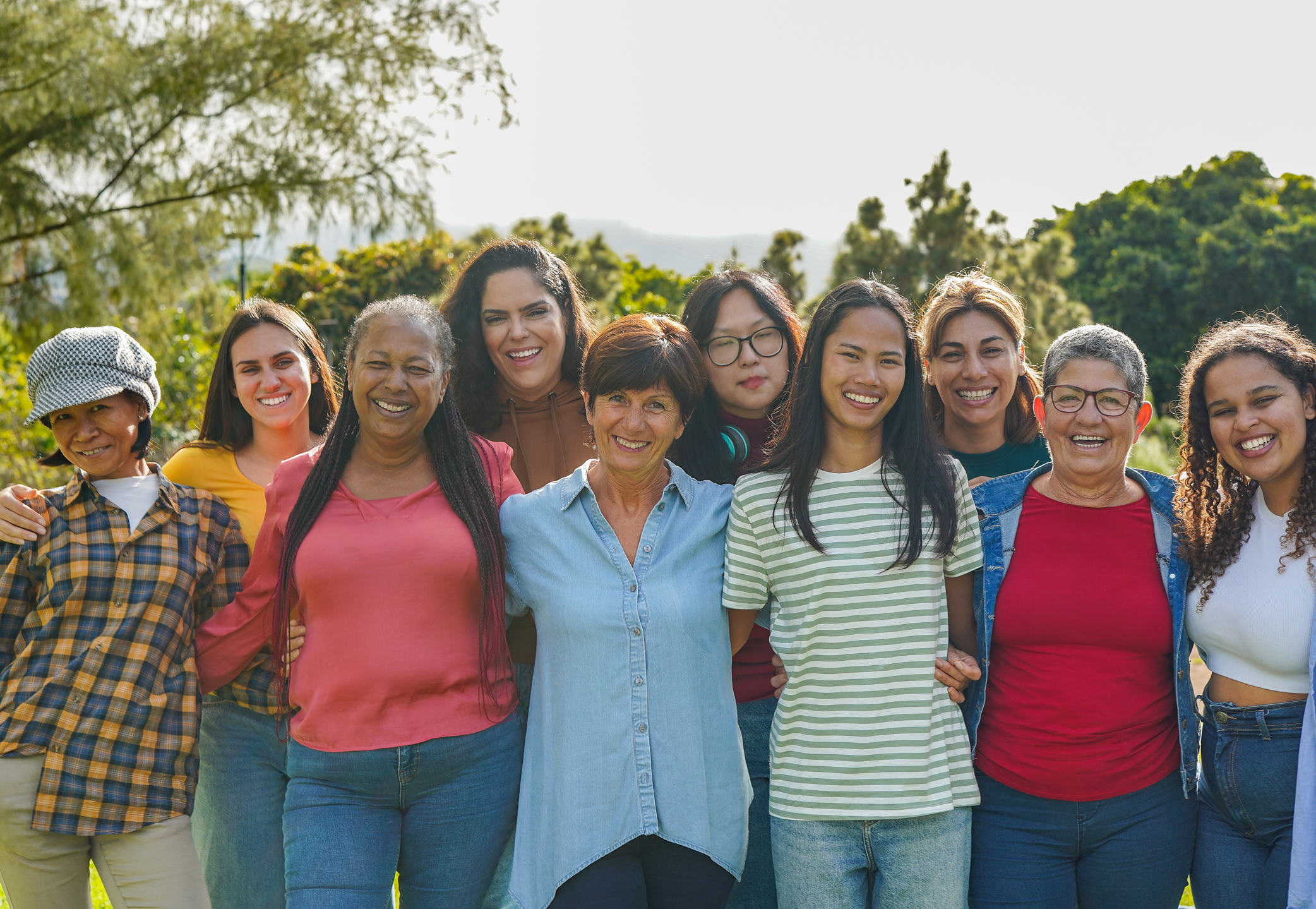 A group of diverse women stand side by side in a park-like setting