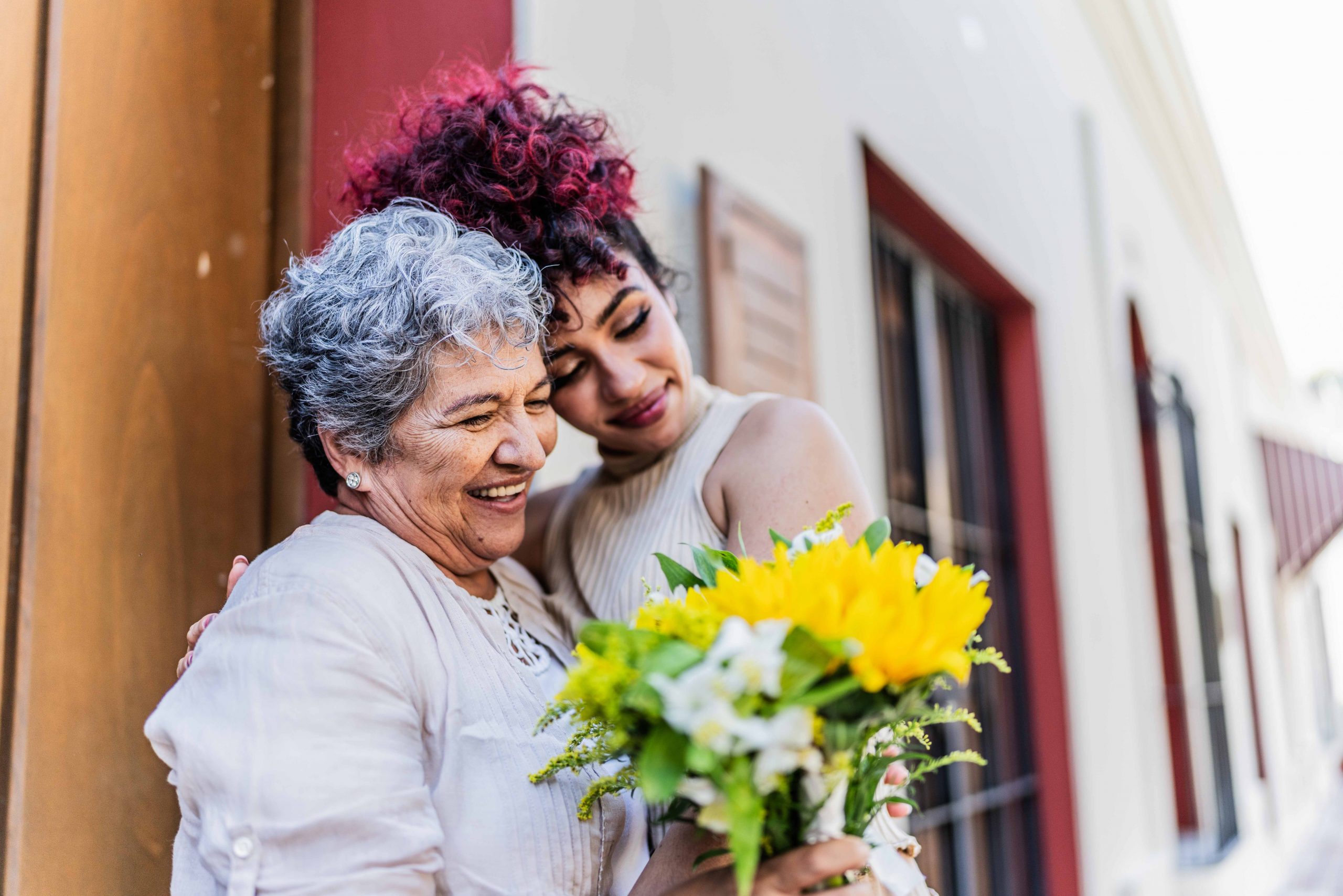 Mother and daughter in embrace outside holding flowers.