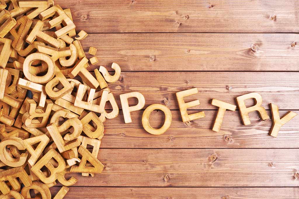 The word poetry made with wooden letters next to a pile of random letters